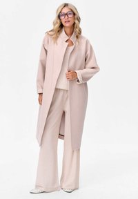 Lange, lichtroze jas met een hoge kraag en een open voorkant, gecombineerd met bijpassende wijde broekspijpen. Zachte textuur, subtiele gestreepte accenten op de mouwen.