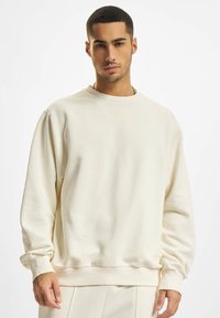 Creme sweatshirt med rund hals, ribbede manchetter og kant, lavet af blødt stof; har et subtilt præget "DEF" logo på forsiden.