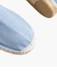 Jasnoniebieskie espadryle z płótna z białym przeszyciem i plecioną jutową podeszwą. Zaokrąglony czubek i fakturowana powierzchnia. Perspektywa z bliska.