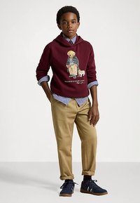 Bordová mikina s potiskem, přeložená přes modro-bíle pruhovanou košili, spárovaná s khaki kalhotami a námořnickými teniskami. Neformální outfit.