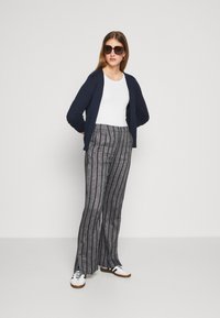 Cardigan marine sur un t-shirt blanc, associé à un pantalon large à rayures grises et des baskets blanches avec des rayures noires. Lunettes de soleil foncées portées.