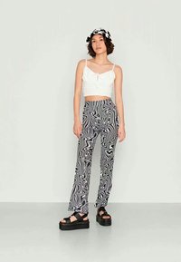 Calças largas com padrão preto e branco, de tecido texturizado, combinadas com um top cropped branco e sandálias de plataforma pretas.