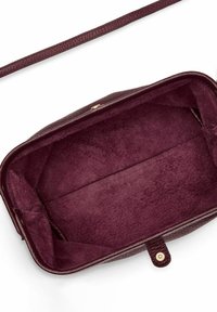 Interno della borsa in pelle bordeaux con rivestimento morbido e texturizzato. Presenta una base piatta e un attacco per una singola tracolla. Nessun compartimento visibile.