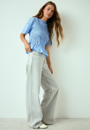 Sinine lühikeste varrukatega pluus kitsaste volditud detailidega, ühendatud heledate hallide laia säärega teksadega. Komplekti kuulub peplum-hõlm ja valged jalanõud.