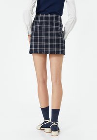 Marineblauwe geruite mini-rok met witte gridlijnen, gestructureerde stof en een aansluitende taille. Gecombineerd met witte hakken en marineblauwe sokken.