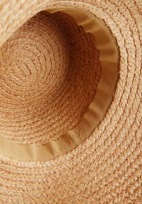 Sombrero de paja de ala ancha en color beige natural, con un patrón tejido texturizado y una banda interior beige con el logotipo "NEXT" en relieve.