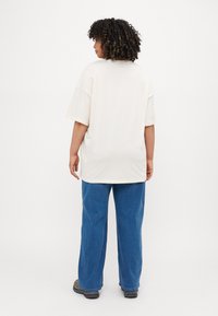 Cream oversized t-shirt with short sleeves, paired with loose blue jeans. Fabric appears soft; no visible patterns or logos.