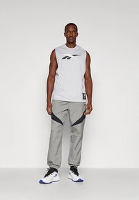 Grå ermeløs treningsskjorte med svart logo, kombinert med grå bukser med mørkeblå detaljer, og hvite sko med blå såler.