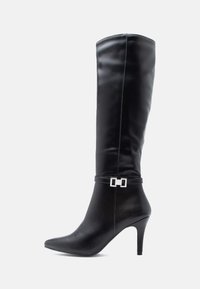Black knee-high boot made of smooth leather, featuring a pointed toe, stiletto heel, and a decorative silver hardware accent on the ankle.