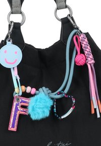 Schwarze Stofftasche mit grauen Trägern, verziert mit bunten Anhängern: einem blauen Smiley-Tag, einem glänzenden pinken 'F', einem flauschigen blauen Pom-Pom und geflochtenen Akzenten.