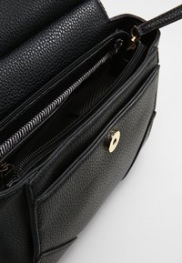 Black textured leather handbag with a zippered main compartment and front pocket, featuring gold hardware and a striped interior lining.