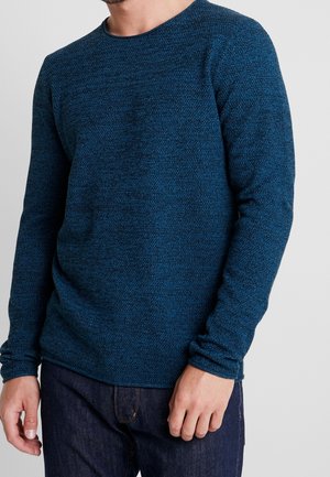 Strukturierter Pullover mit langen Ärmeln in Dunkelblau, mit Rundhalsausschnitt und leicht tailliertem Schnitt, kombiniert mit dunklen Denim-Jeans.