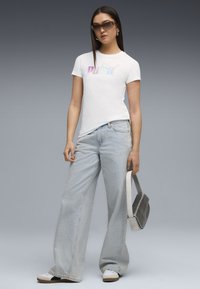 Hvid kortærmet t-shirt med en regnbue-gradient "PUMA"-logo, stylet med lyseblå bredde ben jeans og hvide sneakers.