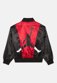 Casaco bomber de satin preto e vermelho com uma silhueta proeminente em preto de um jogador de basquete nas costas e punhos elásticos.