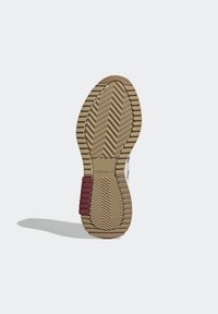 Skoens yttersula har ett fiskbensmönster i brunt gummi med röda accenter. Texturerad yta för grepp och flexibilitet. Varumärkeslogotyp synlig.