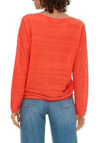 Top lungo a maniche con una vivace tonalità corallo e una trama a coste. Vestibilità comoda con scollo ampio, abbinato a jeans azzurri chiari.