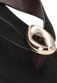 Detalle de zapato de ante negro con un acento dorado brillante y una correa de cuero marrón oscuro. Textura suave con un embellecimiento en forma de lágrima.