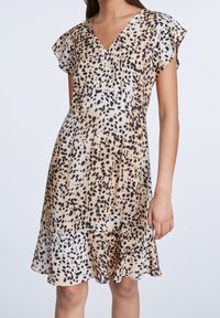 Leopardenmusterkleid in hellbeige und schwarz, mit V-Ausschnitt, schwingenden Ärmeln und ausgestelltem Saum. Glattes Material mit leicht glänzender Struktur.