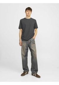 Dunkelgraues Rundhals-T-Shirt kombiniert mit hellblauen, weit geschnittenen Jeans und braunen Sneakers mit weißen Streifen. Schlichter, lässiger Stil.