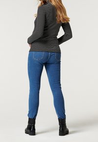 Randig långärmad topp i svart och vitt, kombinerad med tajta blå jeans. Detaljer inkluderar rund hals, smal passform och svarta ankelskor.