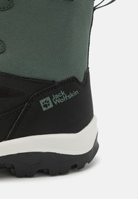 Czarny i zielony but górski z teksturowaną cholewką, wzmocnionym gumowym czubkiem i białą oraz czarną podeszwą. Zawiera logo Jack Wolfskin.