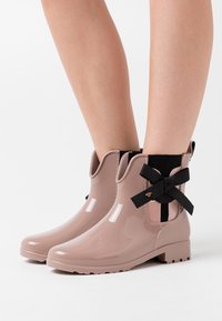 Bottines de pluie rose brillant avec un accent en ruban noir et des panneaux latéraux élastiques, dotées d'une semelle texturée pour une meilleure adhérence.