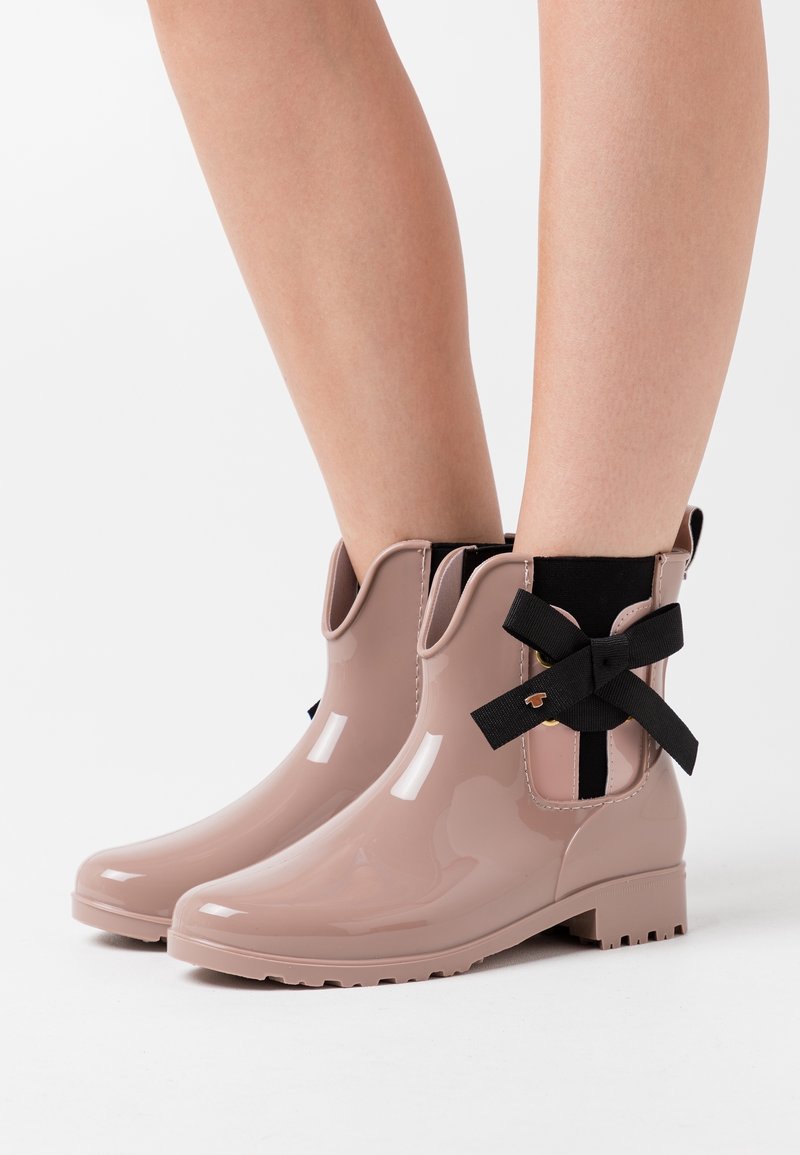 Bottines de pluie rose brillant avec un accent en ruban noir et des panneaux latéraux élastiques, dotées d'une semelle texturée pour une meilleure adhérence.