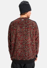 Maglione in pile con motivo rosso e marrone, colletto rotondo, dettagli neri sulle spalle e orlo a costine. Logo sulla parte posteriore del collo.