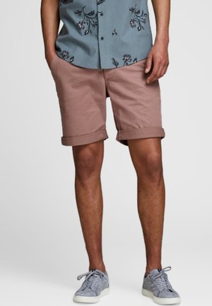 Hellrosa Shorts mit umgeschlagenen Säumen aus Baumwollmaterial, mit glatter Textur und lockerem Schnitt, kombiniert mit einem Hemd mit Blumenmuster.