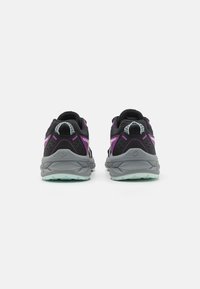 Zapatillas de correr negras y grises con una parte superior texturizada, detalles en morado, elementos reflectantes y una suela exterior verde. Vista trasera que muestra los elementos de diseño.