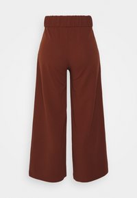 Pantalons amples marron avec une taille élastique. Fabriqués en tissu lisse, présentant un design simple sans motifs ni accents visibles.