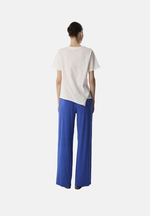 Camiseta blanca de algodón con mangas cortas, combinada con pantalones anchos de pierna amplia en azul real con pliegues. La camiseta tiene un dobladillo ligeramente asimétrico.