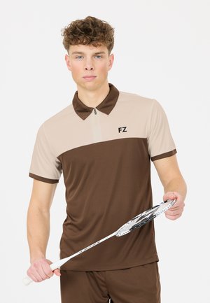 Nuori mies pitää valkoista sulkapallomailaa, yllään ruskea ja beige poolopaita, jossa on "FZ"-logo rinnassa.