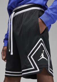 Black athletic shorts with mesh fabric, white accents, and side pockets. Features a Jumpman logo and contrasting hem details.