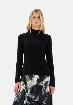 Maglione nero a costine con dettagli a trecce, collo alto e orlo svasato, abbinato a una gonna a fantasia in bianco e nero.