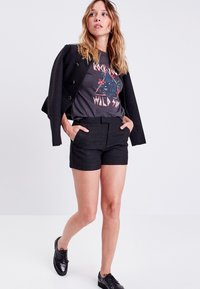 Svart texturerad blazer, grå grafisk t-shirt med färgggrant mönster, svarta skräddarsydda shorts och blanka svarta snörskor. Avslappnad outfit.