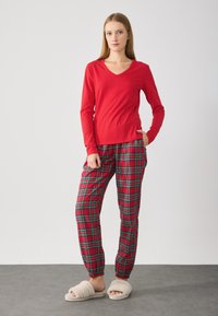 Rød langærmet V-hals top parret med røde plaid bukser med grønne og sorte striber, afsluttet med beige fluffy slidssko.