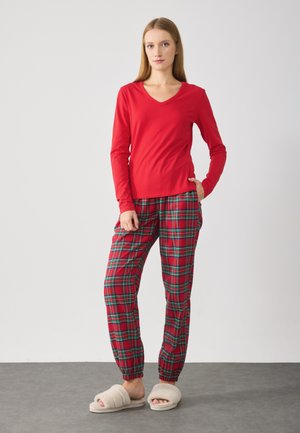 Tricou roșu cu mânecă lungă și decolteu în V, asortat cu pantaloni roșii în carouri cu linii verzi și negre, completat cu papuci pufoși bej.