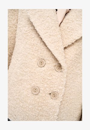 Beige wollen jas met structuur, grote revers en vier bijpassende beige knopen aan de voorkant.