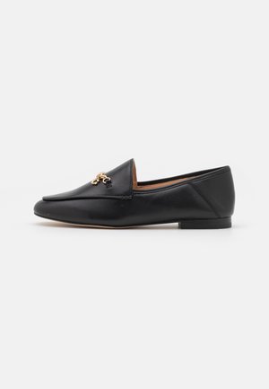Black leather loafers with a flat sole, pointed toe, and a decorative gold emblem on the front. Smooth texture with stitched detailing.