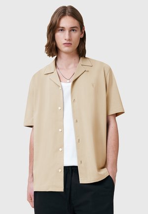 Korte mouw beige shirt van zacht materiaal, met een knoopsluiting aan de voorkant, een puntige kraag en subtiele borduurdetails op de borst.
