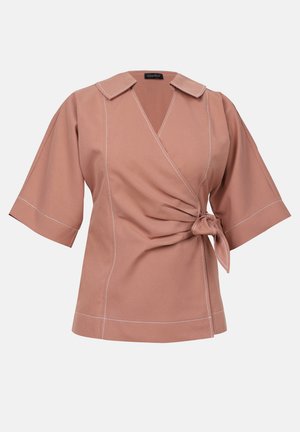Top en wrap rose blush avec col et manches larges, présentant un détail à nouer à la taille et des coutures blanches contrastantes le long des coutures.