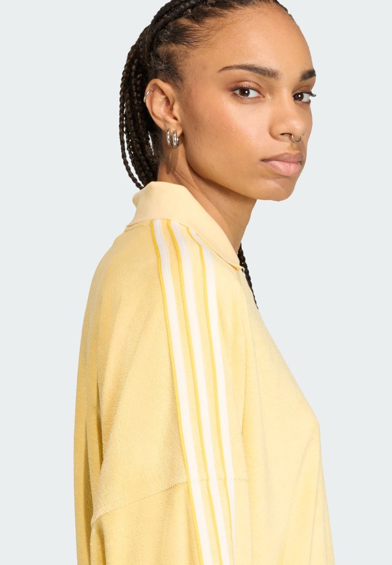 Polo giallo realizzato in tessuto morbido, caratterizzato da una superficie testurizzata, colletto classico e tre strisce bianche sulle spalle.