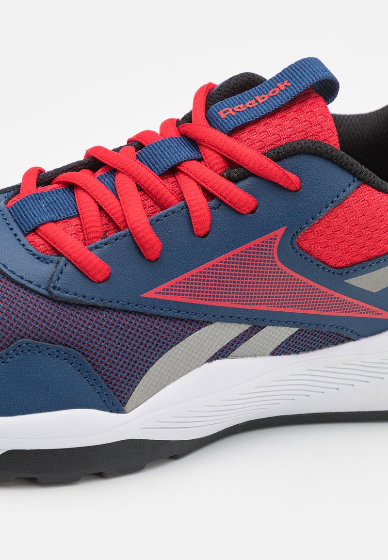 Chaussure de sport bleue et rouge avec tige en maille, lacets rouges, accents gris et semelle blanche. Présente le logo "Reebok" sur la languette.