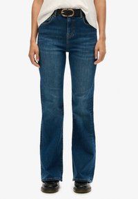 Jeans de campana azules con cintura alta, hechos de denim, con un cinturón negro y una hebilla redonda de plata, textura suave y un ajuste entallado.