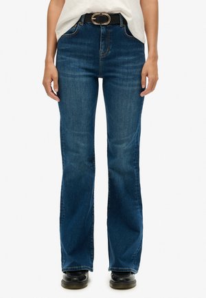 Blaue, aus Denim gefertigte Schlagjeans mit hoher Taille, versehen mit einem schwarzen Gürtel mit einer runden silbernen Schnalle, glatter Textur und taillierter Passform.
