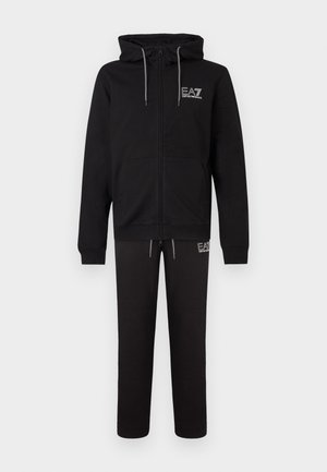 Must kapuutsiga lukuga dressipluus hallide paeltega, esitaskud ja logo. Sobitatud mustade pükstega, millel on elastne vöökoht ja logo.