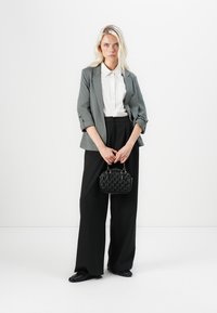 Šedý blazer přes bílou košili, černé široké kalhoty, černou texturovanou kabelku a černé boty na bílém pozadí.
