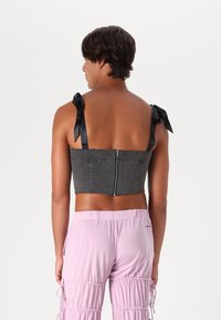 Čierny denimový crop top so zipsom na chrbte a dvoma saténovými stužkami na každom ramene, spárovaný so svetloružovými g gathered nohavicami.