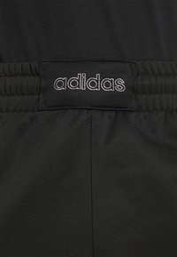 Černé sportovní šortky s elastickým pasem. Na tmavém štítku je bíle vyšitý znak "adidas". Hladký materiál, minimalistický design.
